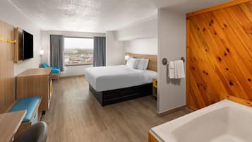 A hotel room with a bed, a desk with a chair, a TV, a window with curtains, and a wooden wall panel.