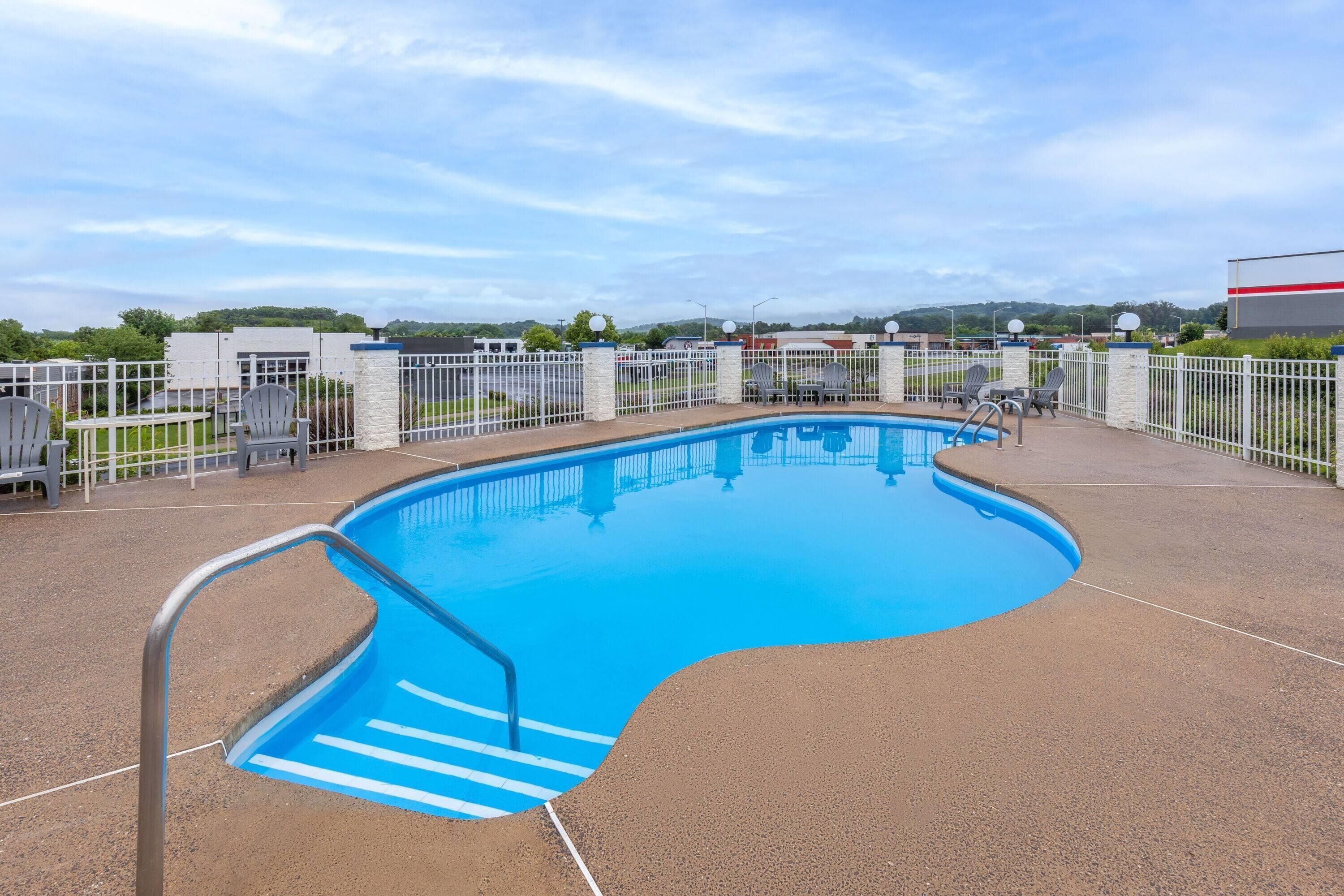 A swimming pool with a metal ladder, surrounded by a white fence and chairs.