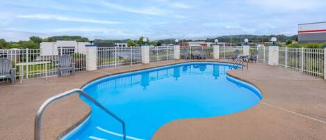 Una piscina con una escalera metálica, rodeada por una valla blanca y sillas.