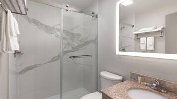 A modern bathroom with a glass-enclosed shower, a white toilet, and a granite countertop sink.