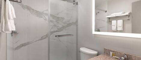 A modern bathroom with a glass-enclosed shower, a white toilet, and a granite countertop sink.