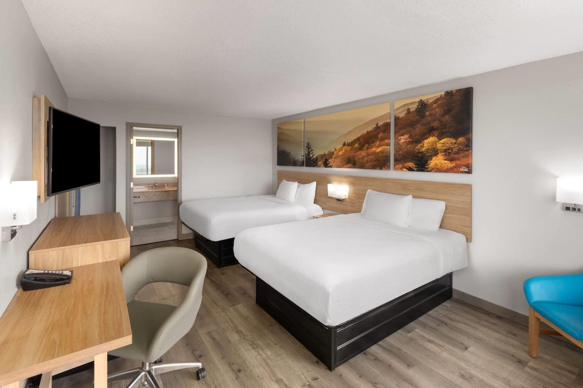 A hotel room with two beds, a desk, a chair, a TV, and a large painting on the wall.