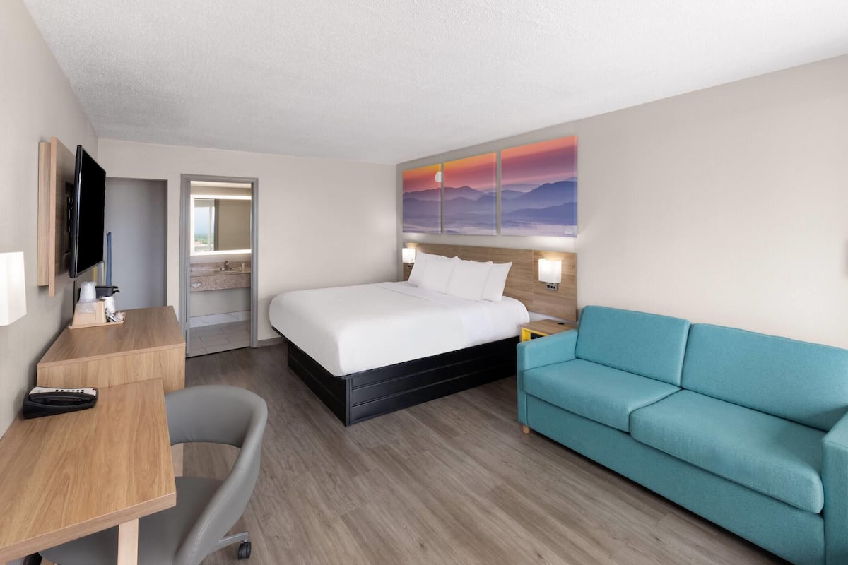 A hotel room with a bed, a desk, a chair, a sofa, and a TV.