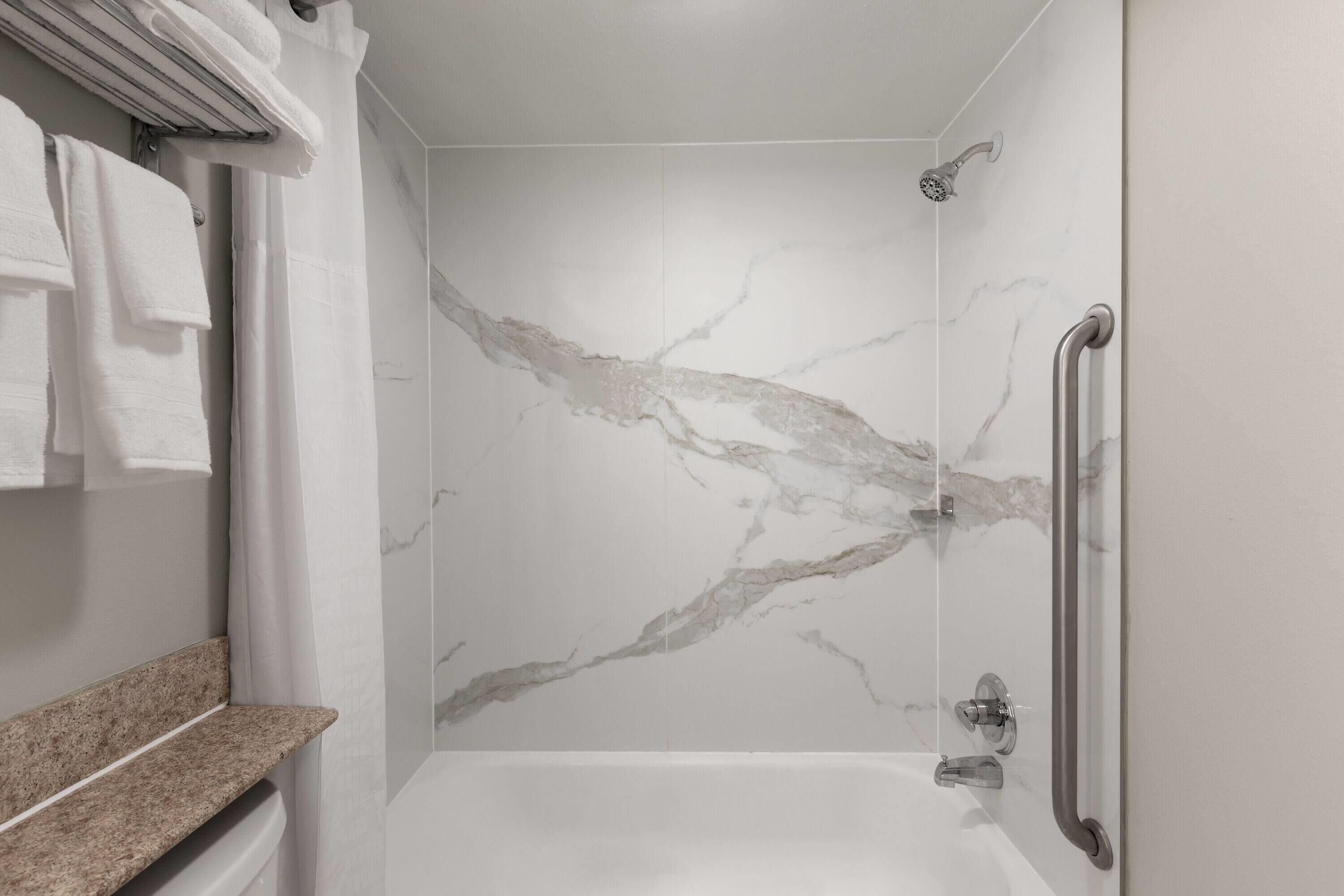 A modern bathroom with a marble shower wall, a built-in bench, and a handrail.