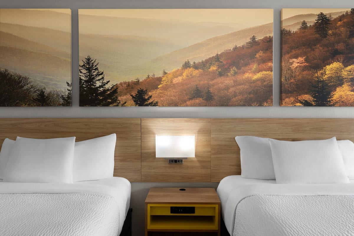 A hotel room with two beds, a nightstand, and a wall-mounted light.