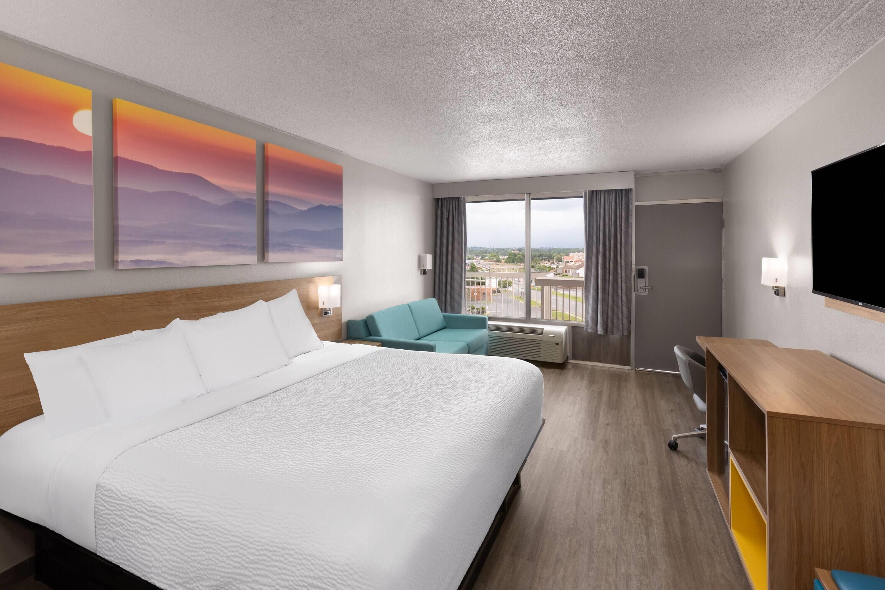 Habitación de hotel con una cama grande, un escritorio, una silla, un televisor y una ventana con vistas a edificios.