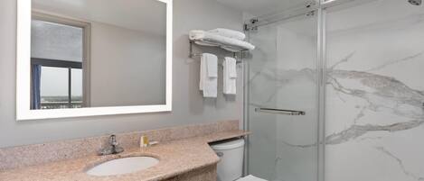 A modern bathroom with a granite countertop sink, a toilet, a glass-enclosed shower, and a large mirror.
