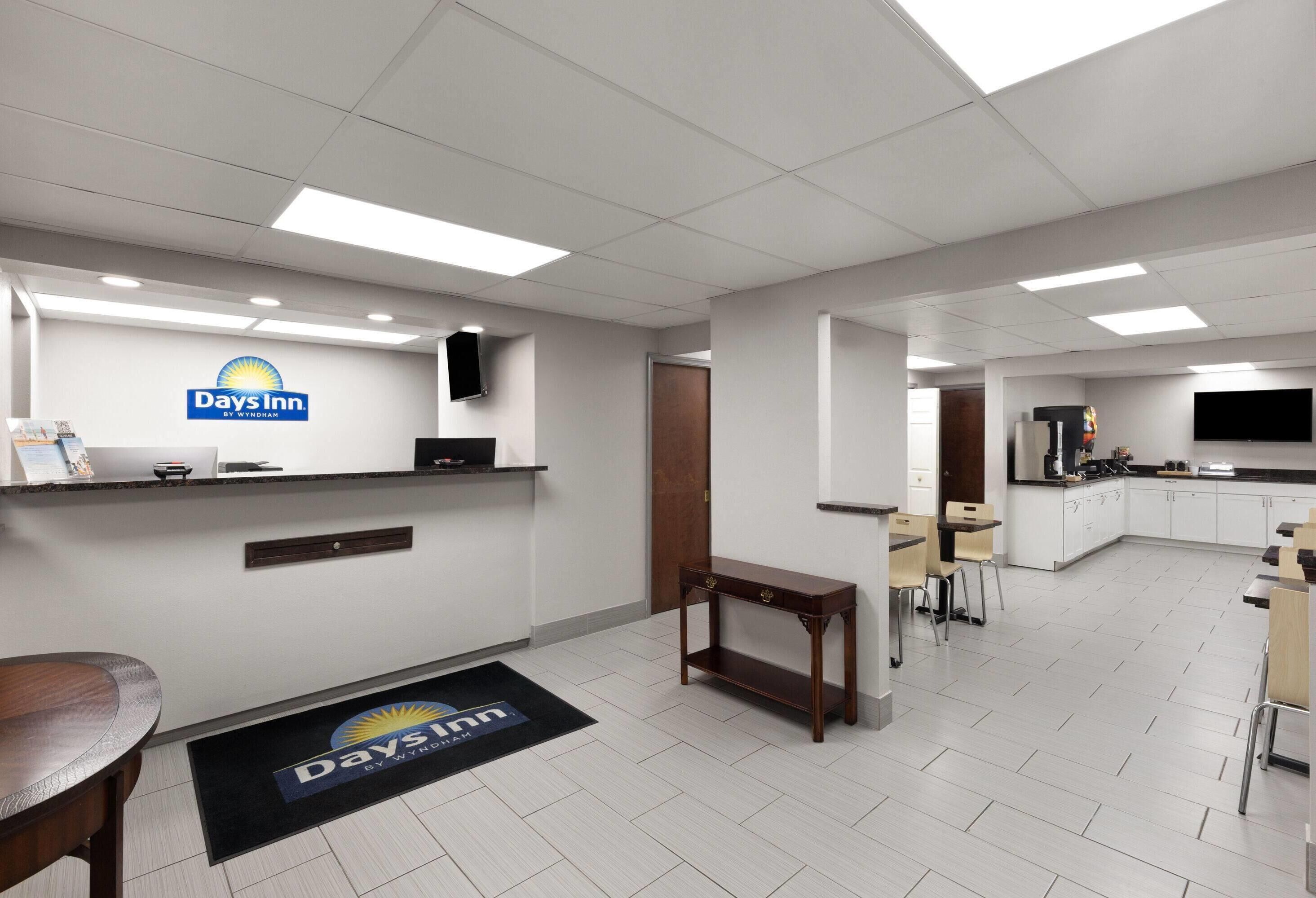 A Days Inn reception area with a reception desk, a flat-screen TV, and a small seating area with chairs and a table.