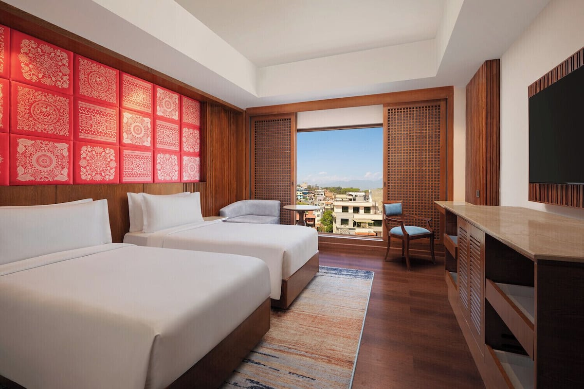 A hotel room with two beds, a desk, a chair, a TV, and a city view.