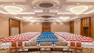 A conference room with rows of white chairs, a stage, and a seating area with sofas and chairs.