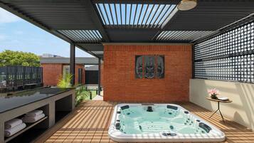 A modern outdoor hot tub area with a wooden deck, a brick wall, and a pergola overhead.