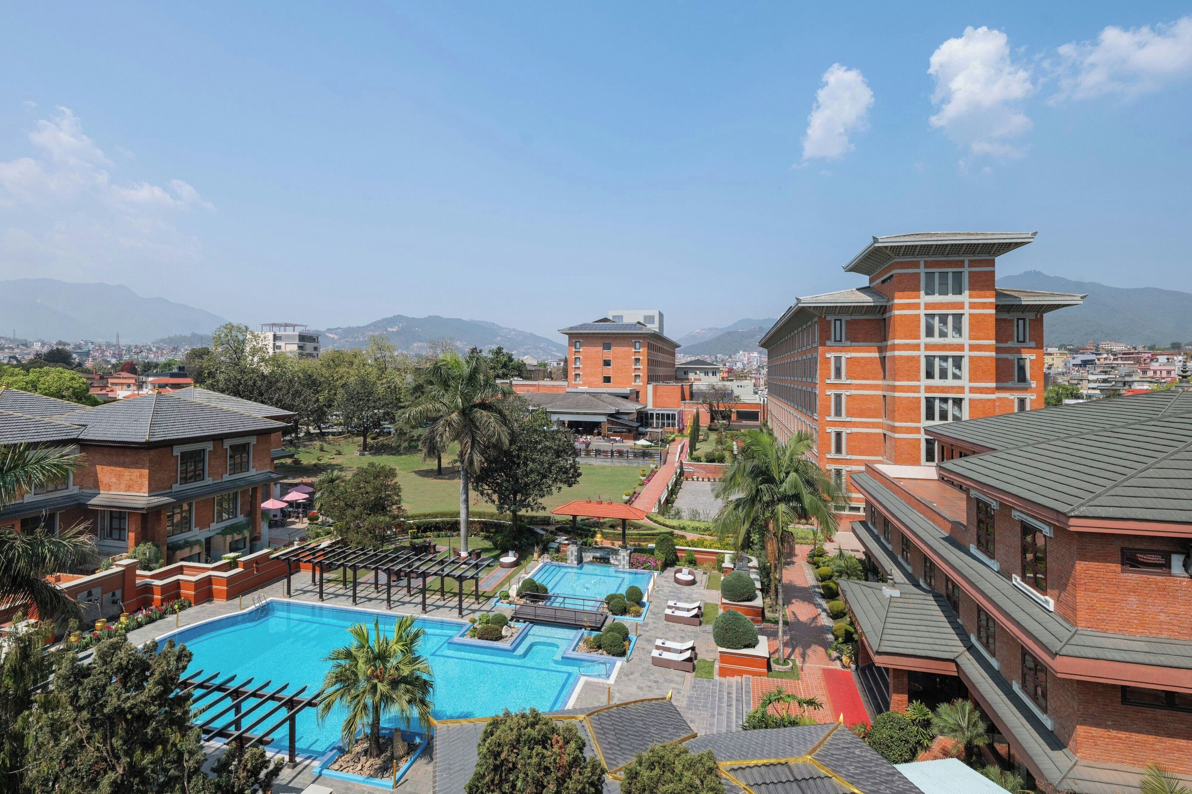 Un hotel con piscina, varias edificaciones y montañas al fondo.