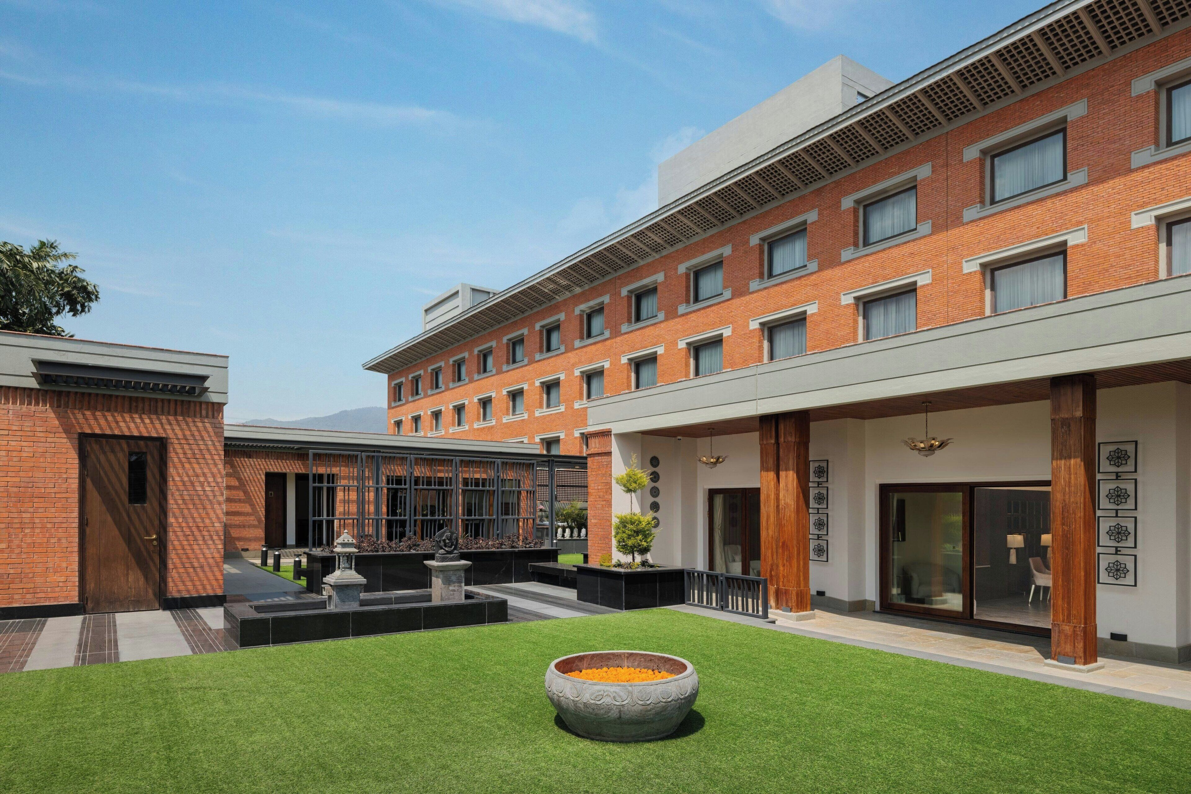 A modern building with a brick facade, large windows, and a courtyard with artificial grass and a decorative bowl.