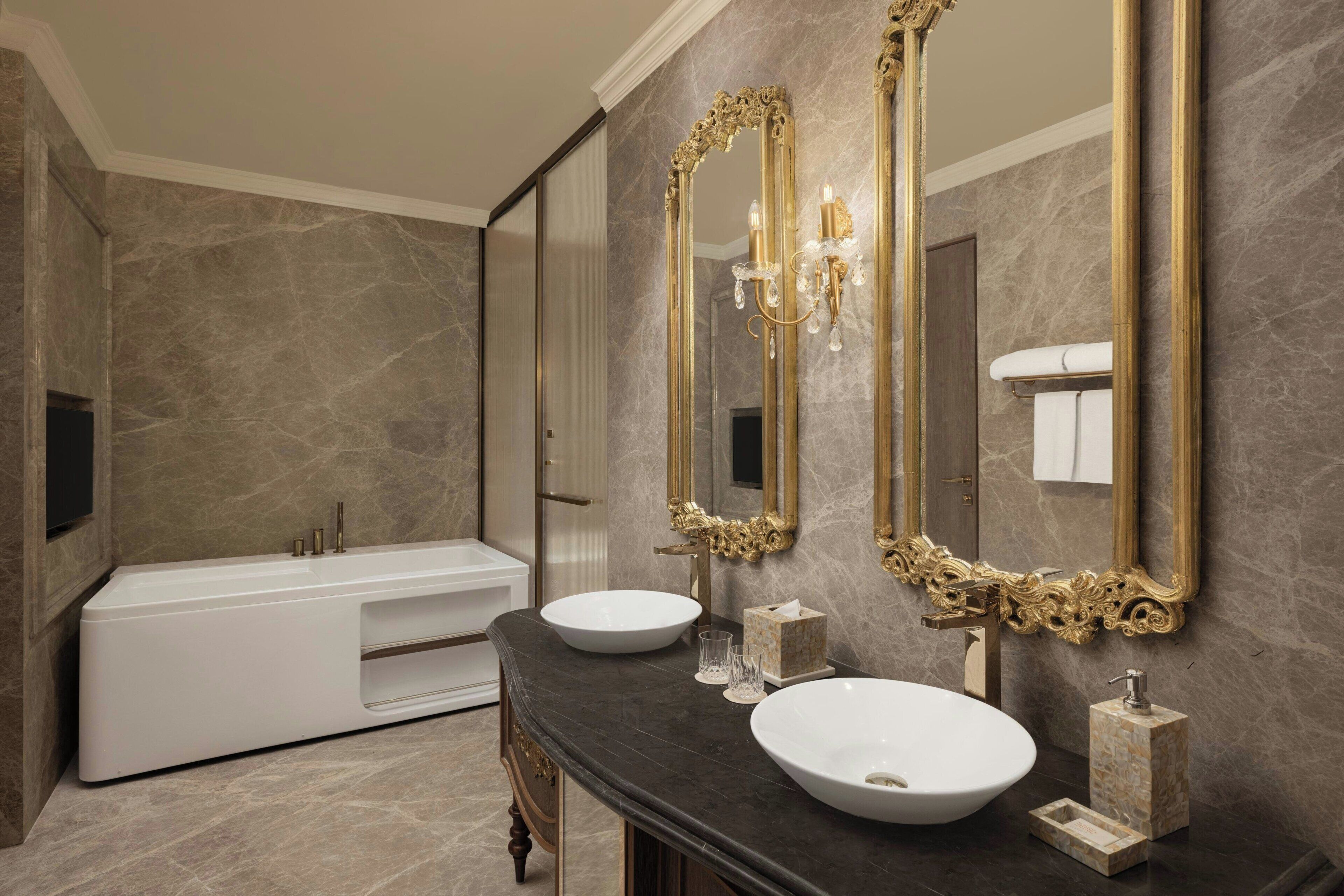 A modern bathroom with a bathtub, two sinks, and ornate mirrors.