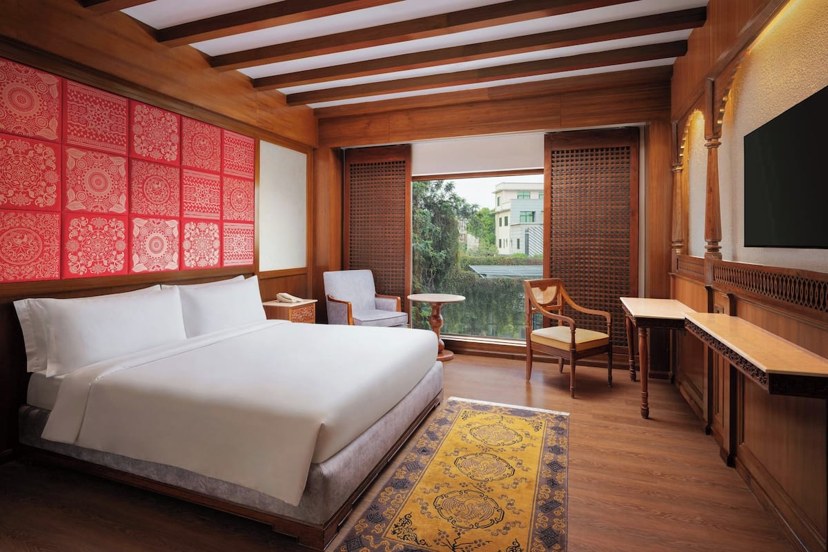 A hotel room with a large bed, a desk, a chair, and a view of the outside.