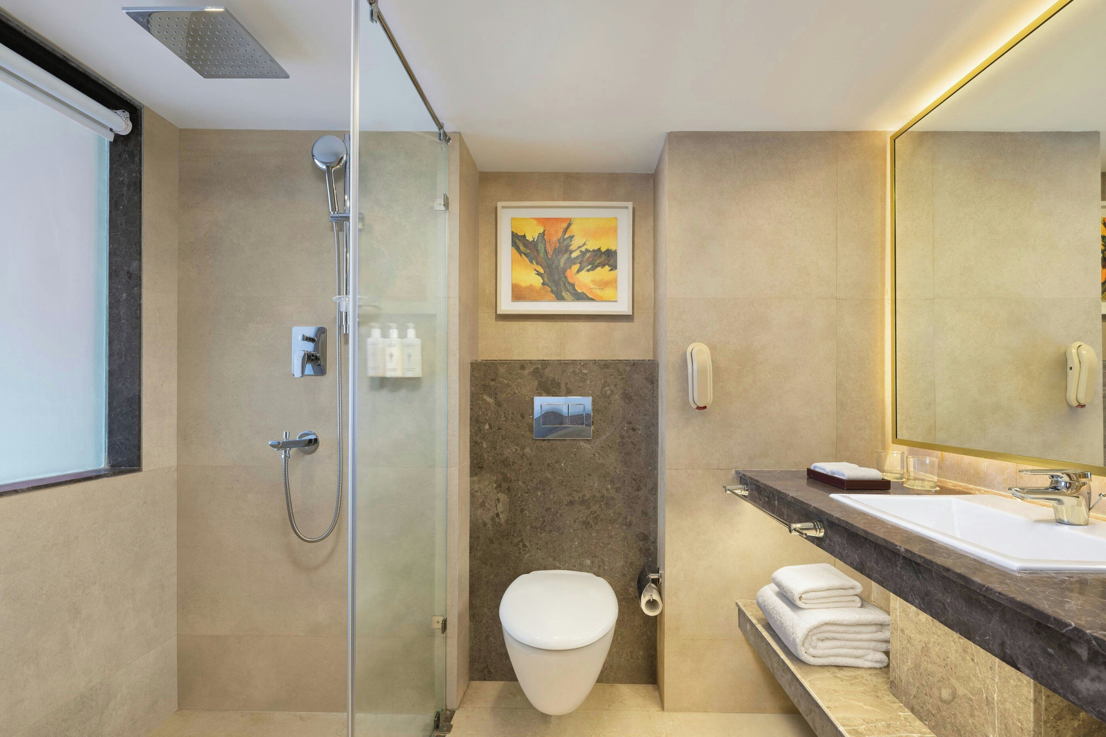 Un baño moderno con ducha de vidrio, inodoro blanco, espejo grande y encimera de mármol.