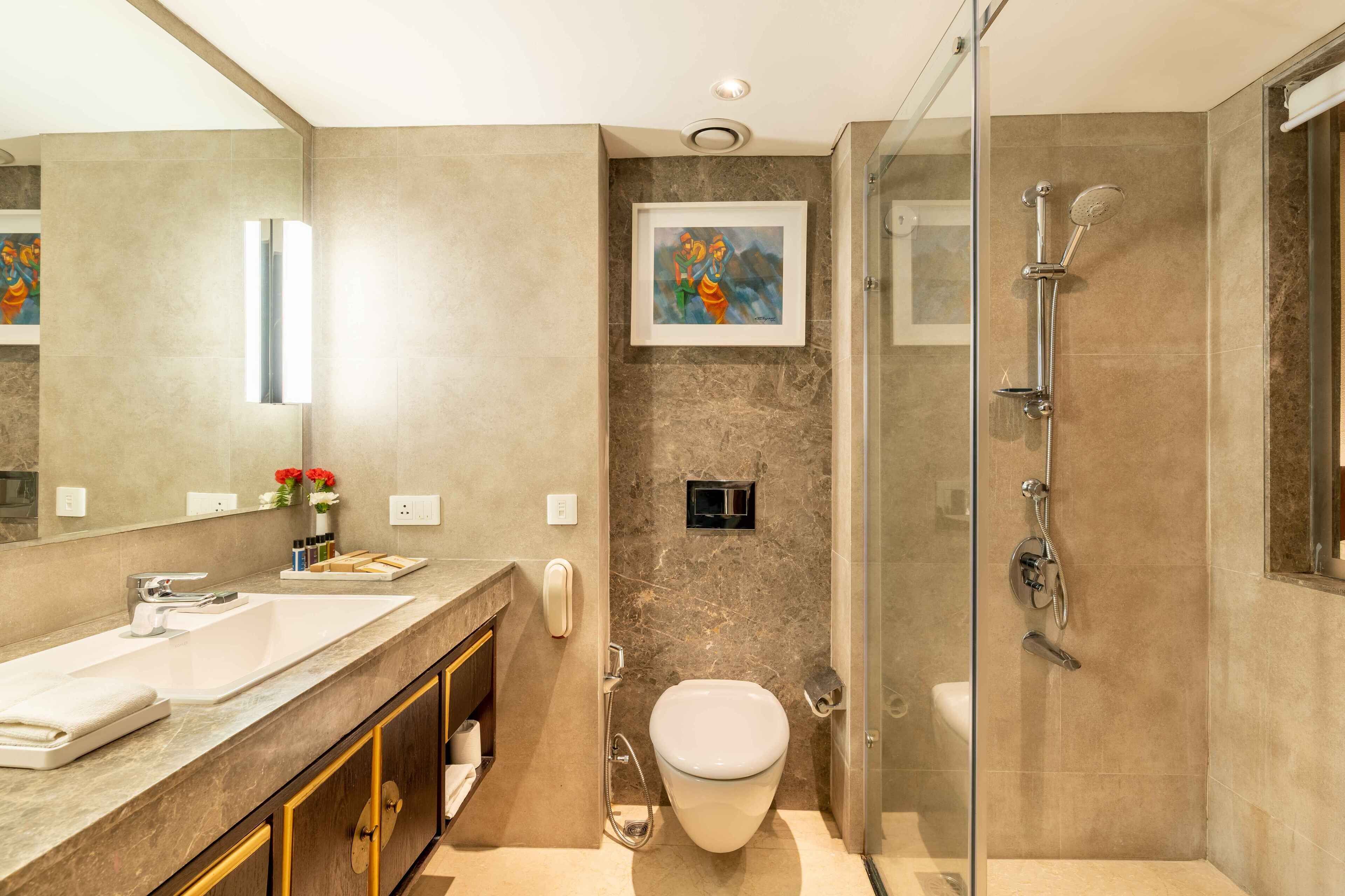 Un baño moderno con un espejo grande, un lavamanos, un inodoro y una zona de ducha.