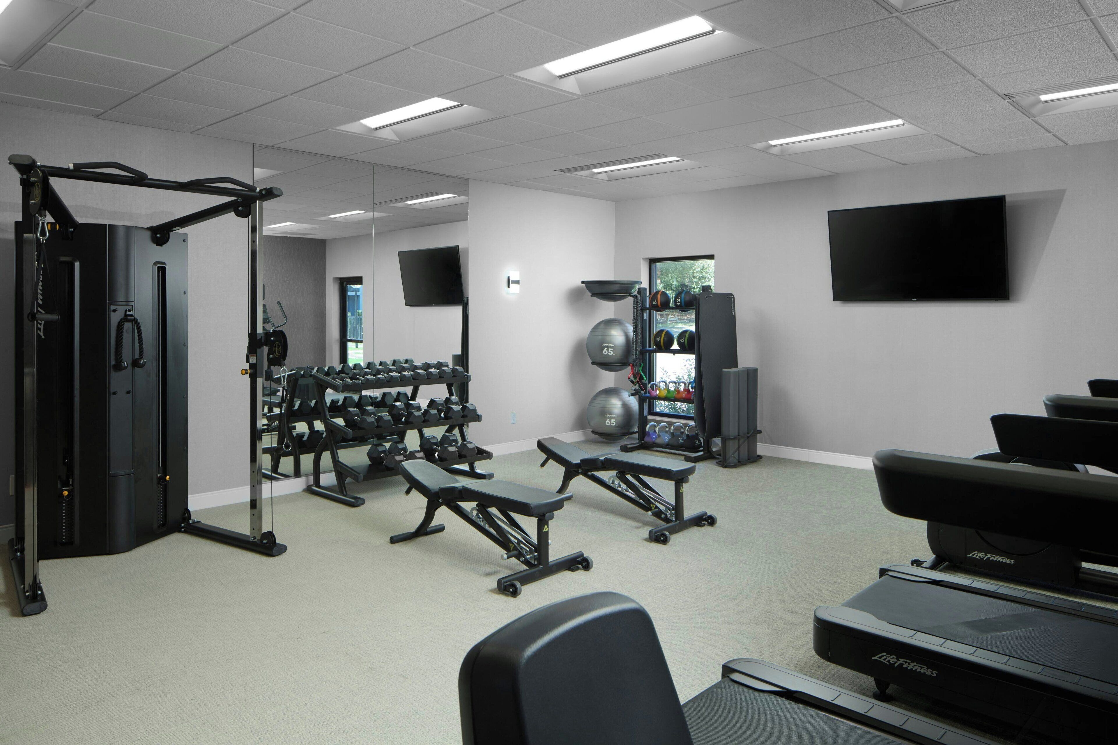Un gimnasio con equipo de ejercicio, pesas, cinta de correr y una pantalla de televisión.