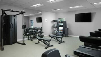 Un gimnasio con equipo de ejercicio, pesas, cinta de correr y una pantalla de televisión.