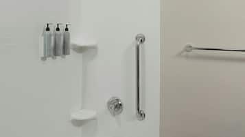 Une salle de bain moderne avec une baignoire, une pomme de douche, une barre d’appui et des articles de toilette rangés sur une étagère.