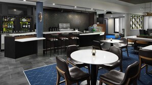 Zona de bar moderna con mostrador, taburetes y un área de estar con mesas redondas y sillas.