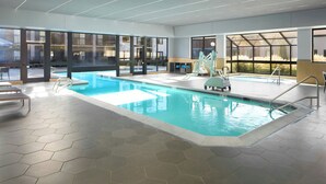 Una piscina interior con paredes de vidrio transparente, suelo de baldosas hexagonales y un tobogán.