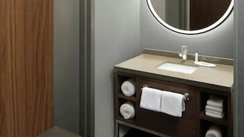 A modern bathroom with a wooden vanity, a round mirror with integrated lighting, and neatly folded towels.