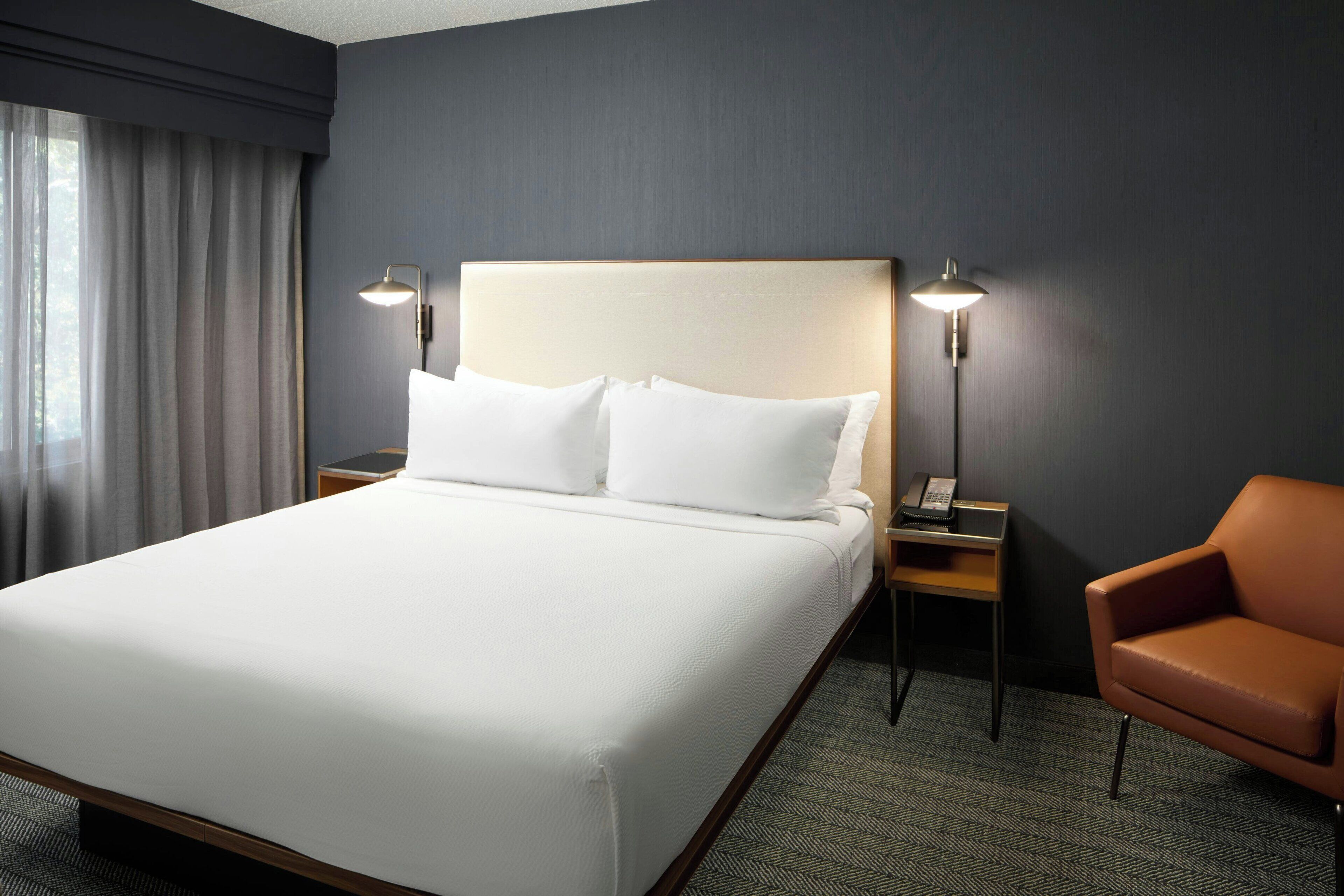 A hotel room with a large bed, two bedside lamps, a chair, and a nightstand with a phone.