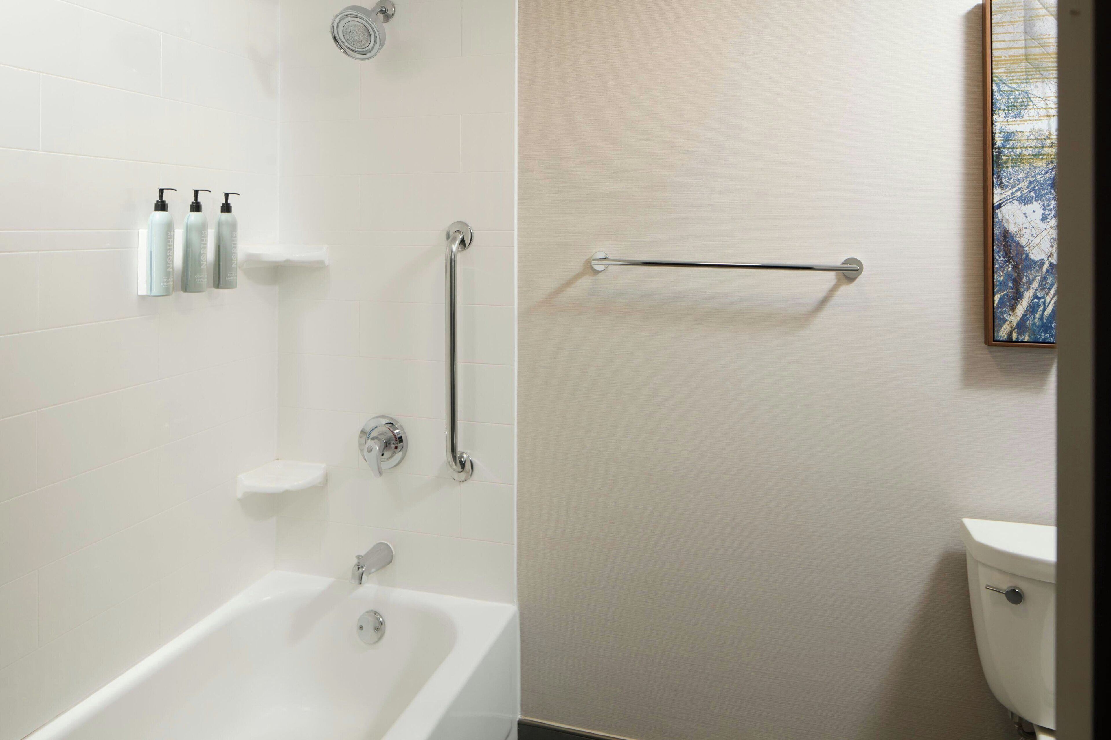 A modern bathroom with a bathtub, a toilet, and a handrail.