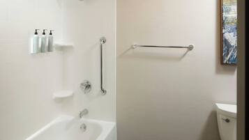 A modern bathroom with a bathtub, a toilet, and a handrail.