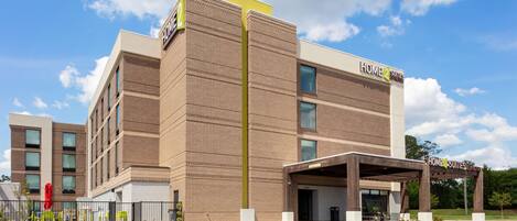 A hotel with a modern brick facade, a covered entrance, and a sign indicating "Home2Suites."