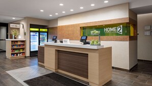 Zona de recepción de un hotel con mostrador, minibar, refrigerador y un pequeño arreglo de plantas.