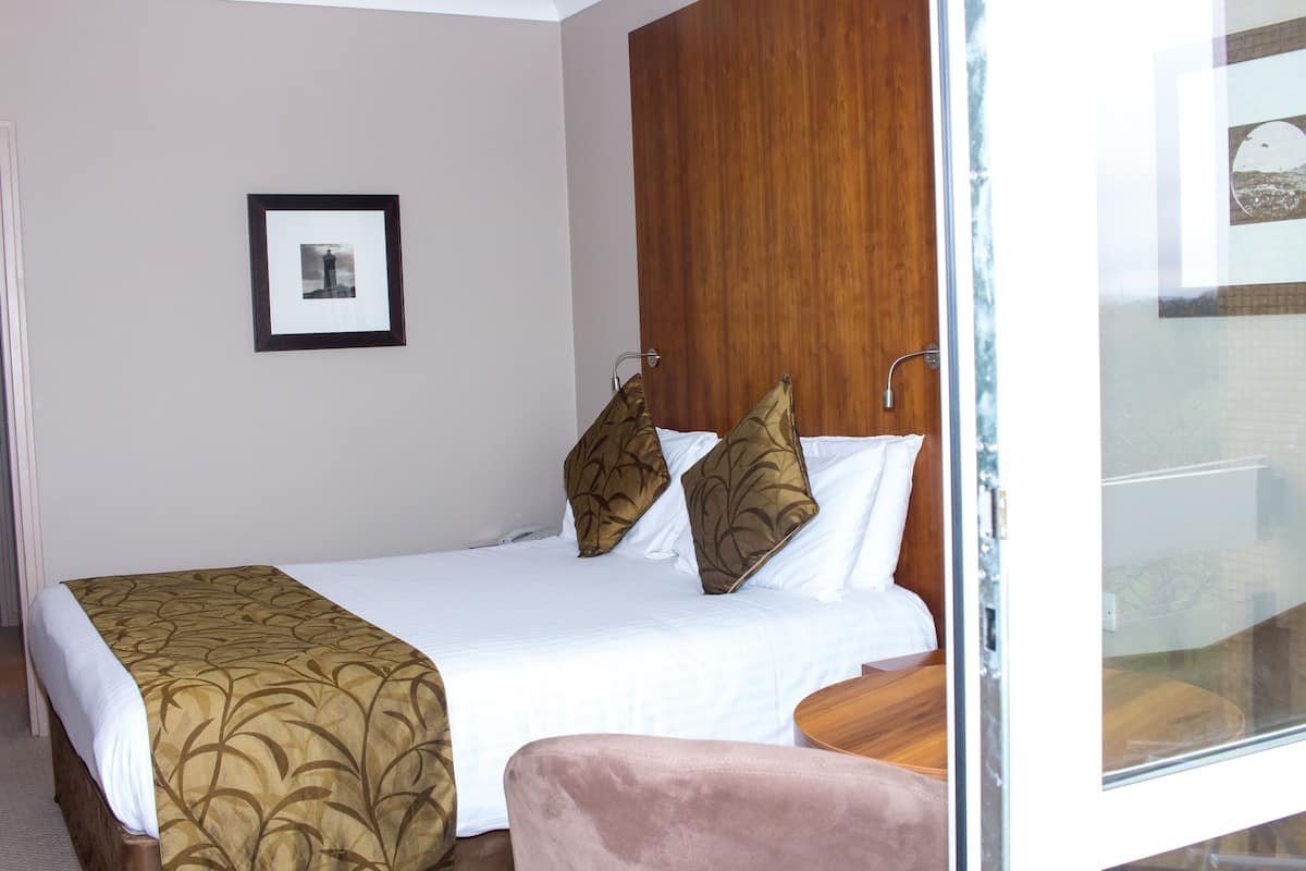 Une chambre d’hôtel avec un lit, une table de chevet, une chaise et un tableau encadré au mur.
