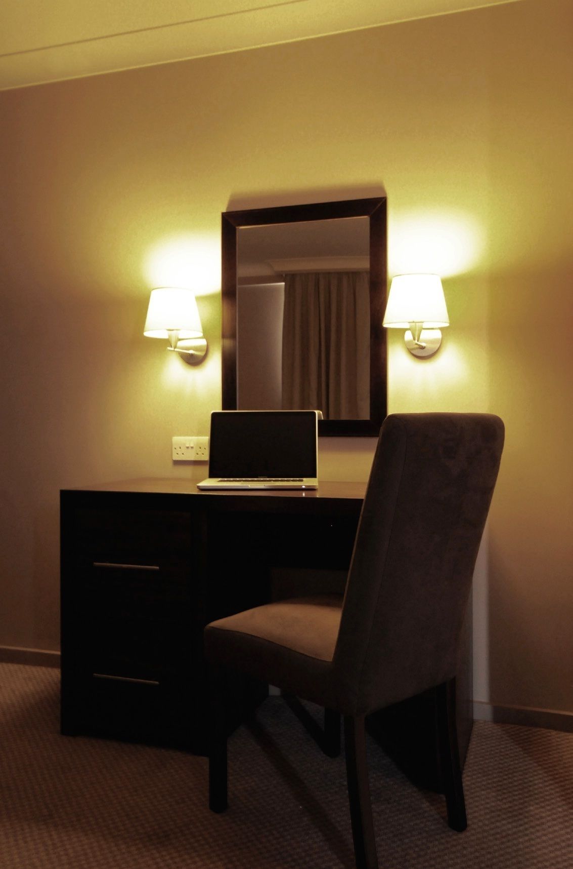 Een hotelkamer met een bureau, een stoel, een laptop en twee wandlampen.
