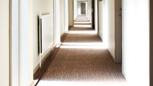 Un pasillo largo y estrecho en un hotel, con piso alfombrado y paredes blancas.