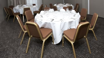 A conference room with round tables, brown chairs, and white tablecloths.