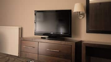 A television on a wooden cabinet with two drawers, a remote control, and a wall-mounted lamp.