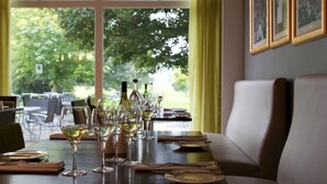 Mesa lista para comer con copas y botellas de vino, un sofá y vistas al exterior con vegetación.