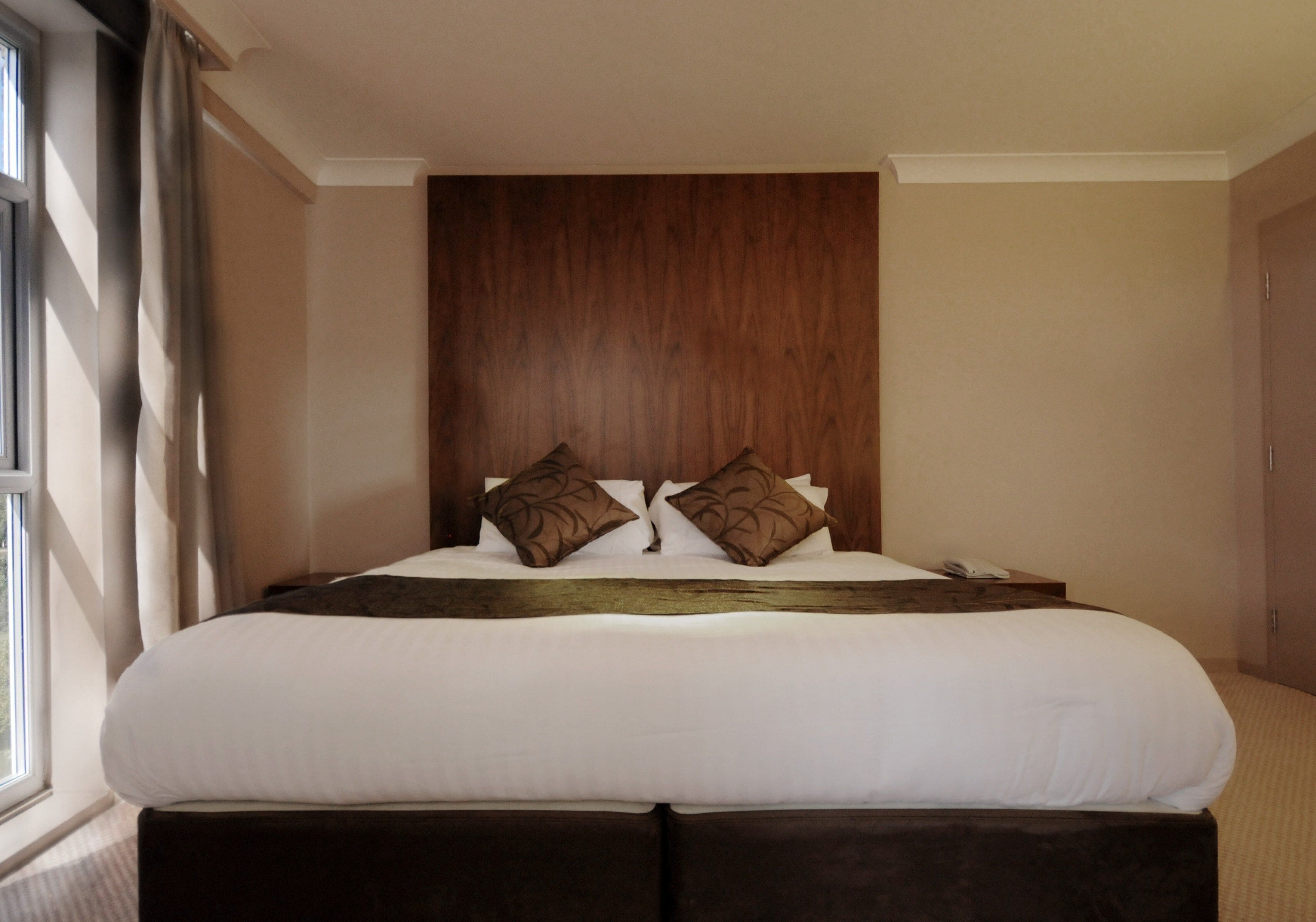 A hotel room with a large bed, a wooden headboard, and a window with curtains.
