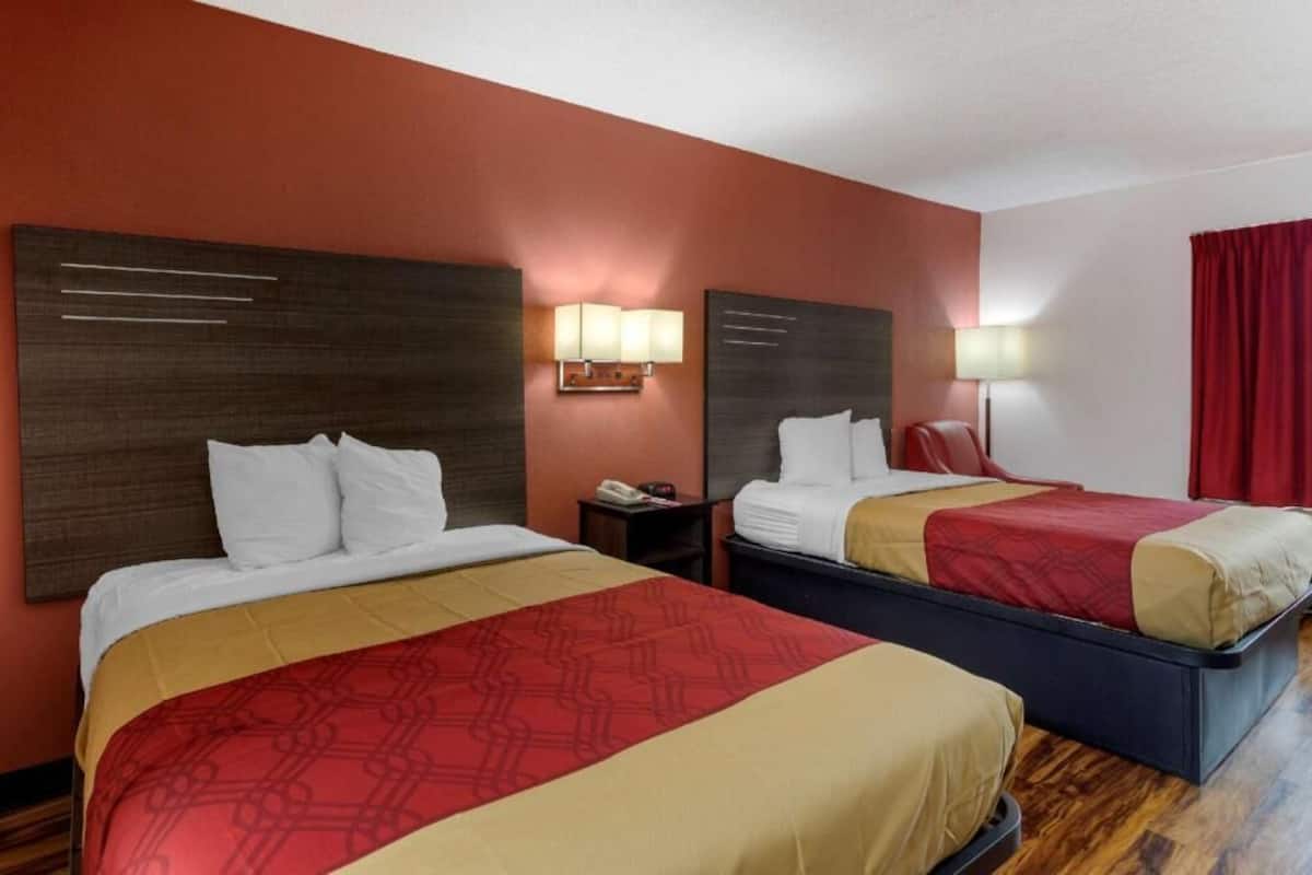 A hotel room with two beds, a wooden headboard, bedside lamps, and a red curtain.