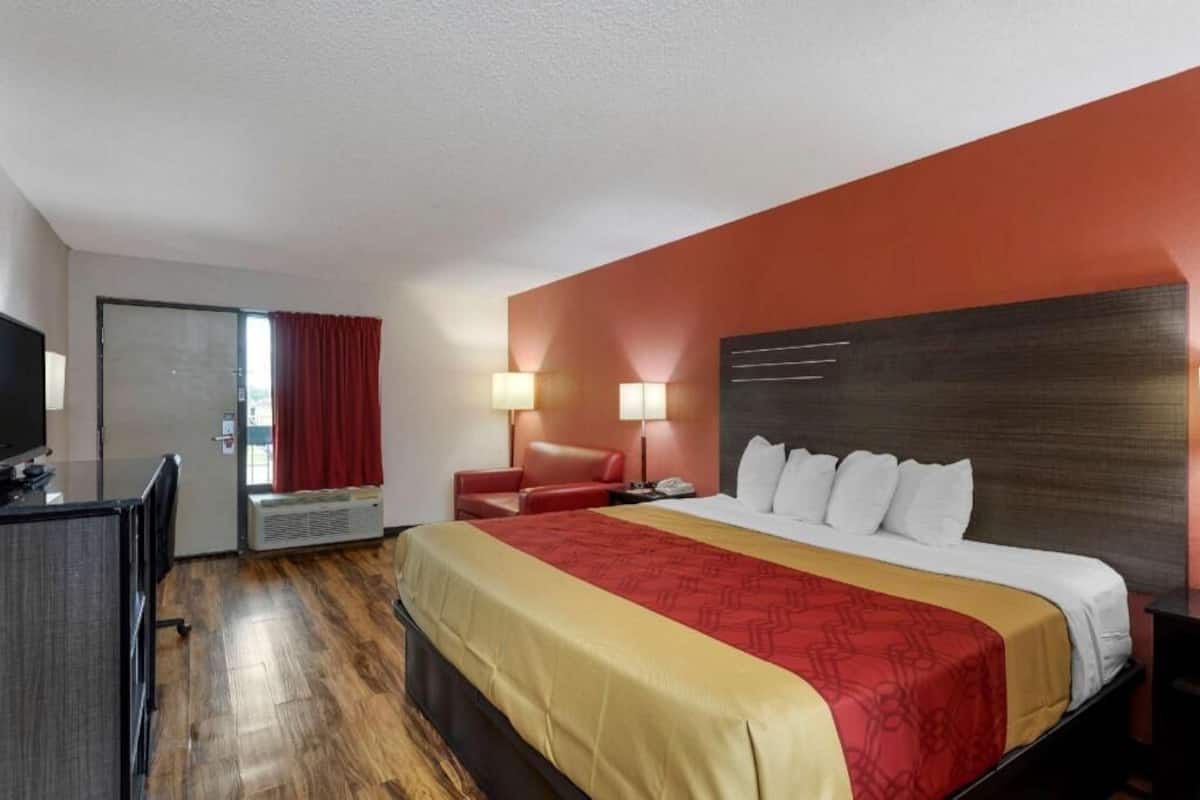 A hotel room with a bed, a desk, a chair, and a television.