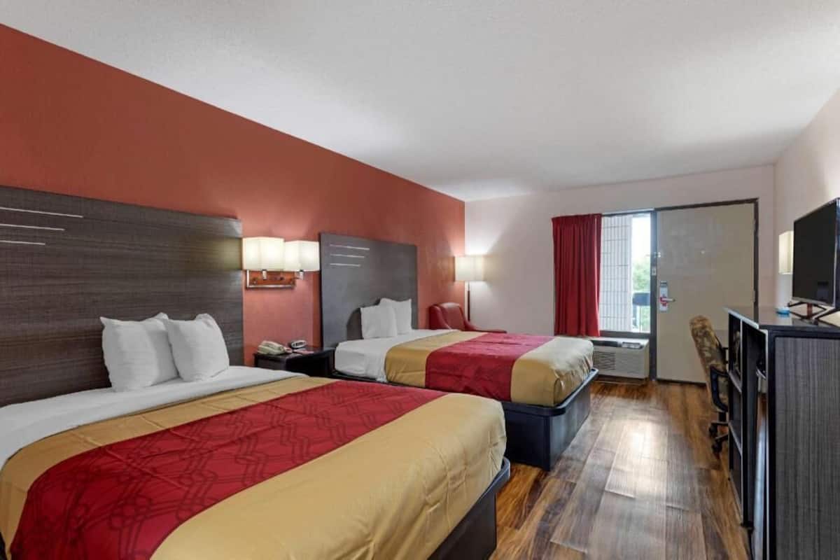 A hotel room with two beds, a desk, a TV, and a window with curtains.