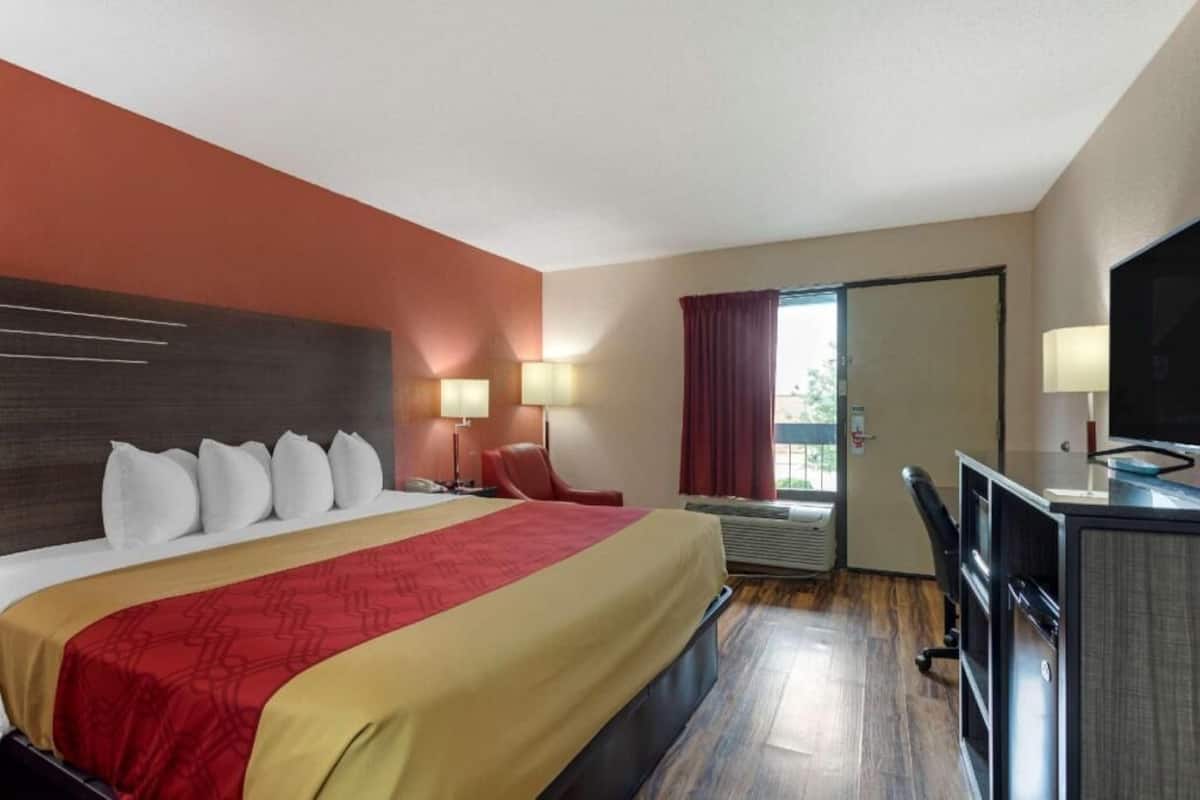 A hotel room with a bed, desk, chair, TV, and a window with curtains.