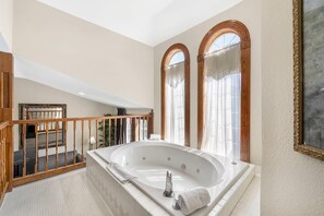 A spacious bathroom with a large bathtub, wooden staircase, and arched windows. - Quality Inn Eureka Springs South (Eureka Springs)