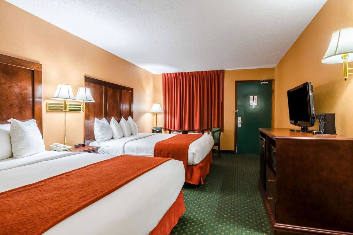 A hotel room with two beds, a desk with a TV, a coffee machine, and a green door.