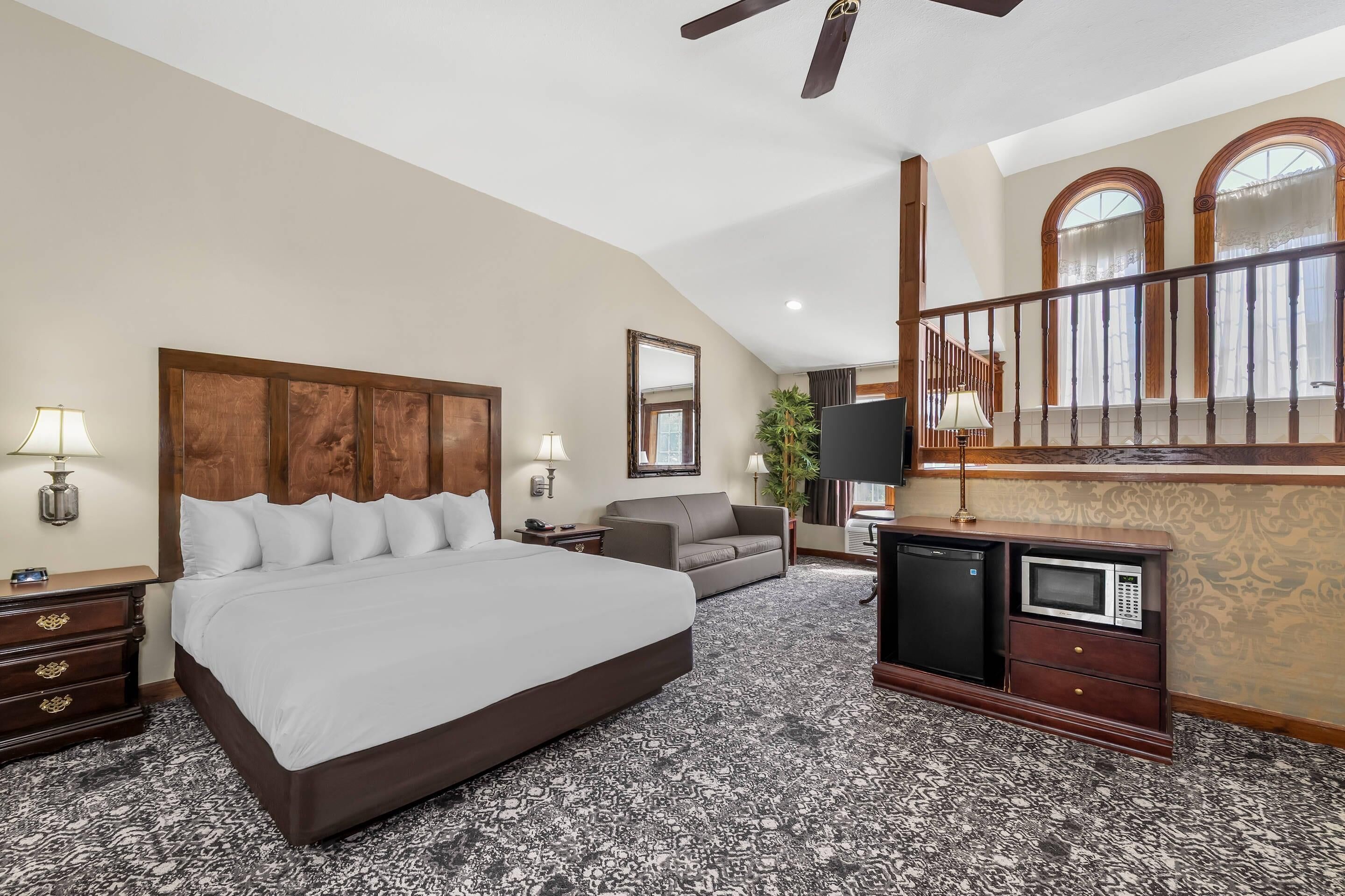 Une chambre d’hôtel avec un grand lit, un canapé, un bureau avec une télévision, un four à micro-ondes et un ventilateur de plafond.