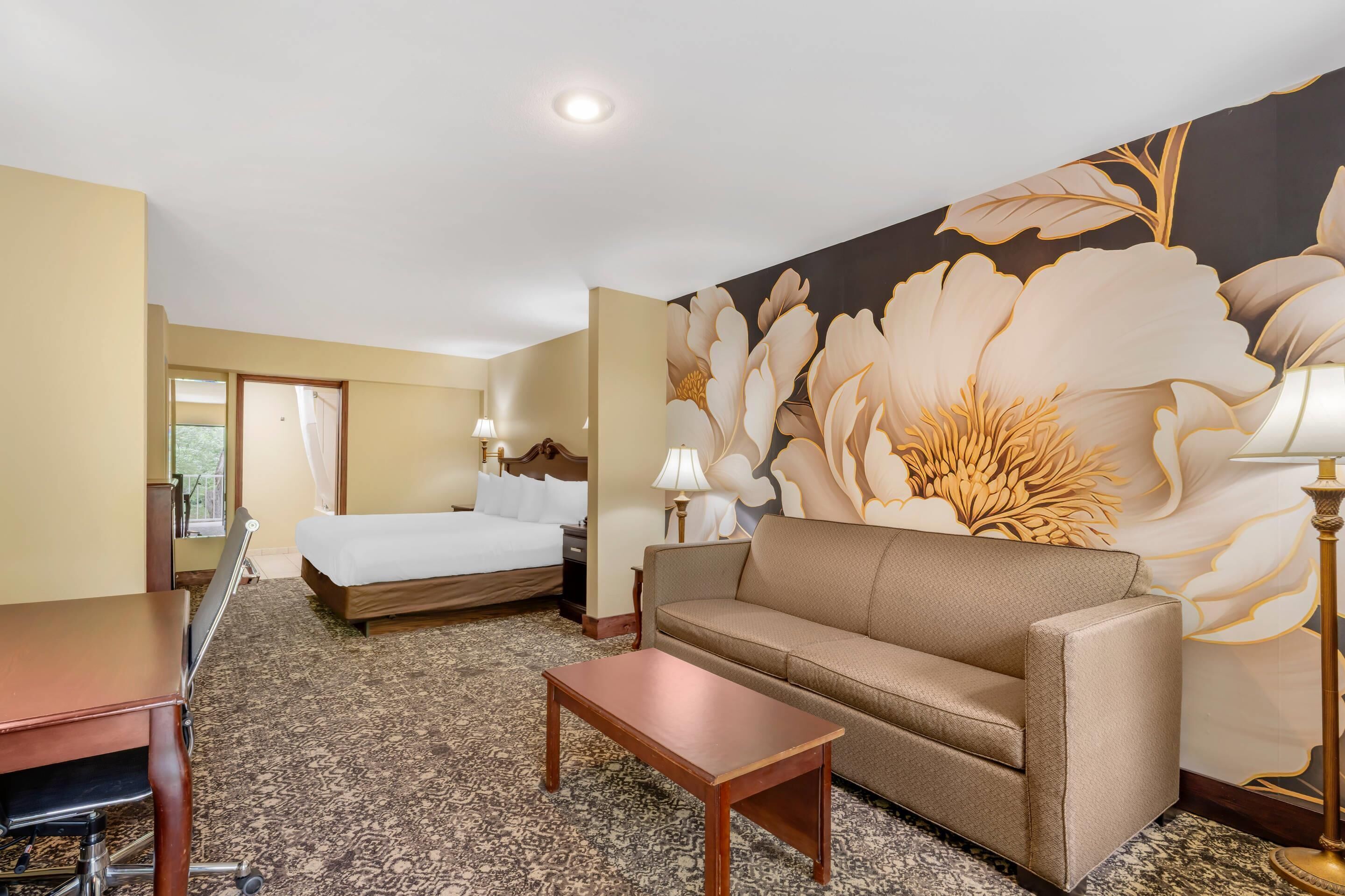 Habitación de hotel con cama, sofá, mesa y un amplio mural floral en la pared.
