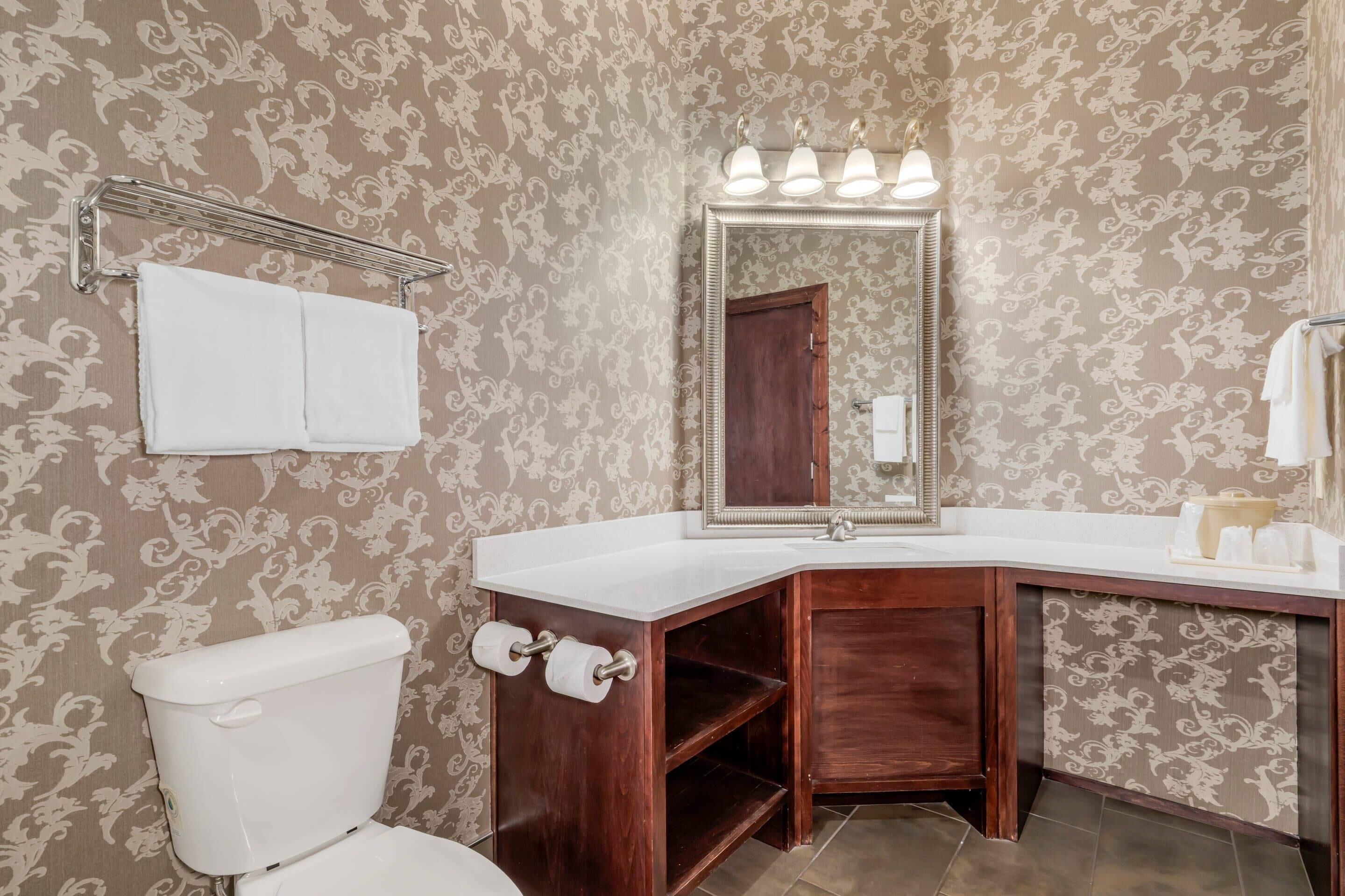 Un baño con inodoro, lavamanos con espejo y perchero para toallas.