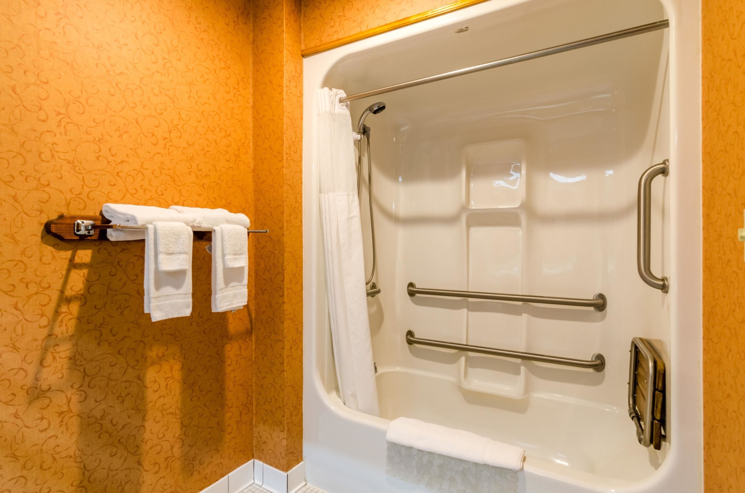 A bathroom with a bathtub, grab bars, and a towel rack with towels.