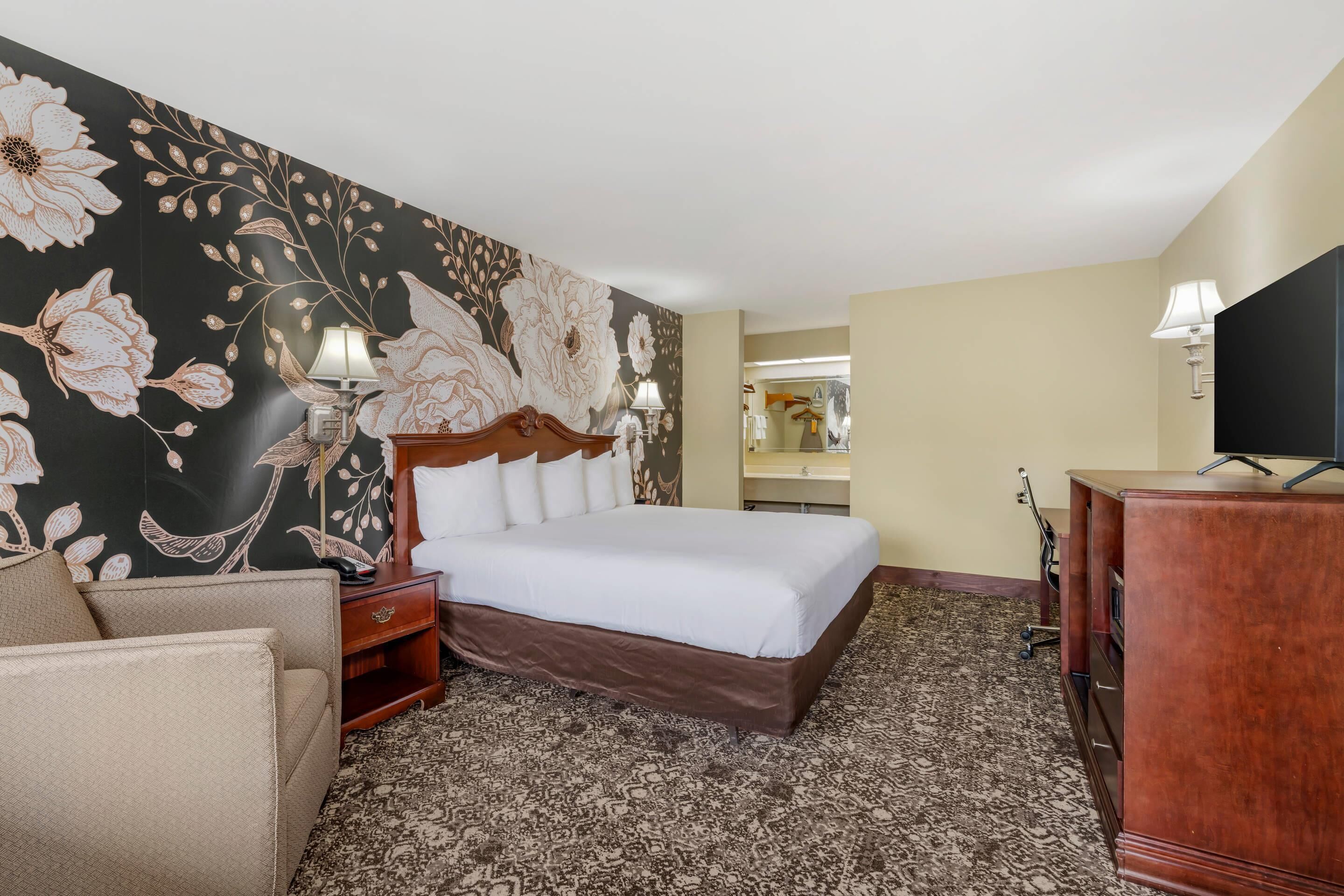 A hotel room with a large bed, two bedside tables with lamps, a wooden dresser, and a large mirror.